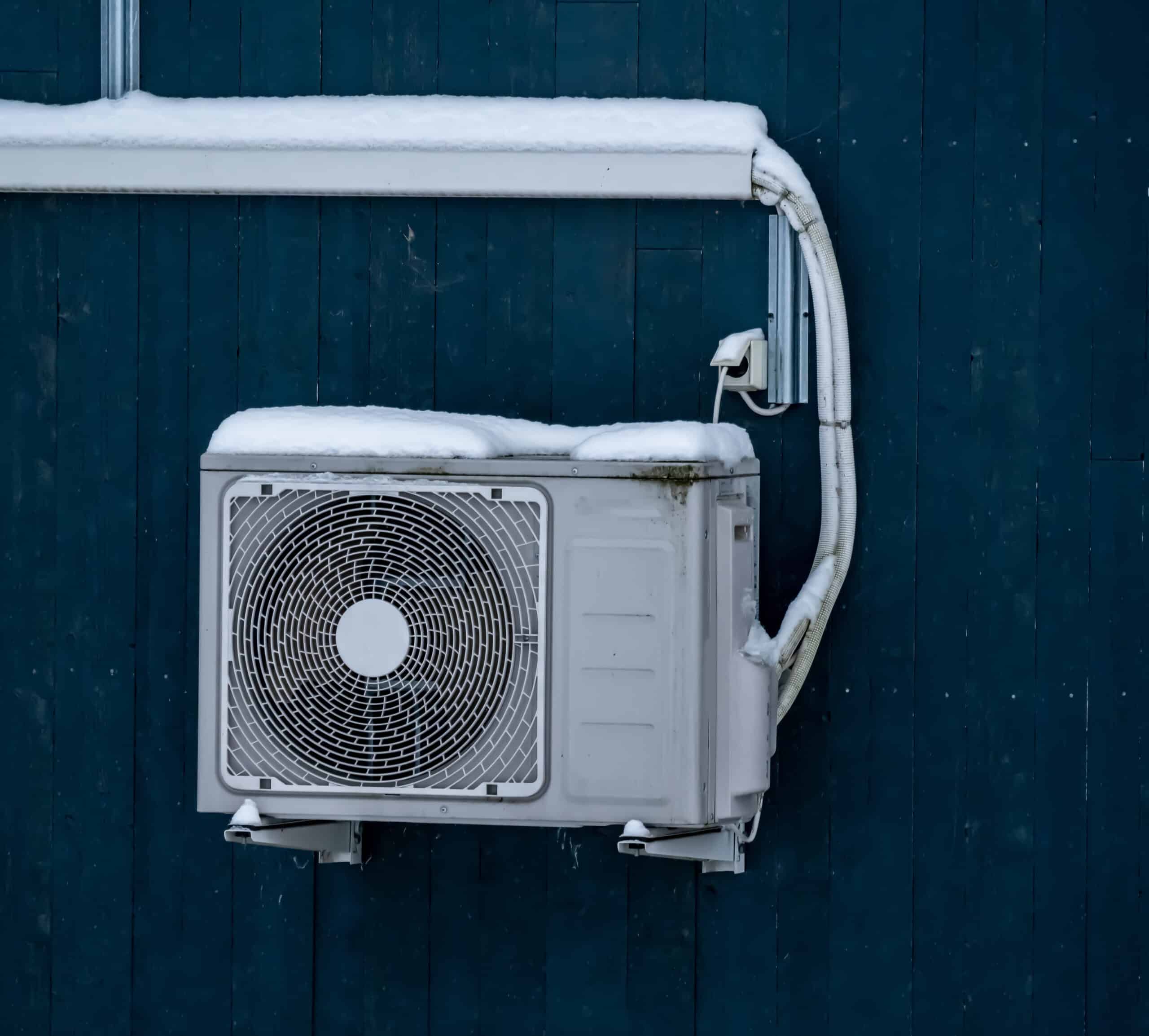 Snow-covered heat pump mounted on an outside wall