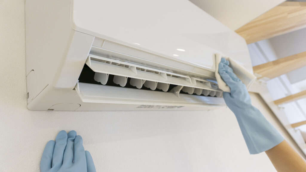 A person wearing rubber gloves cleaning the face of a ductless mini-split unit